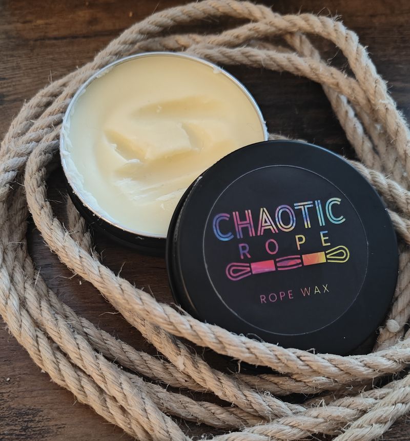 An open tin of Chaotic Rope Wax next to its lid, on a coil of natural jute rope